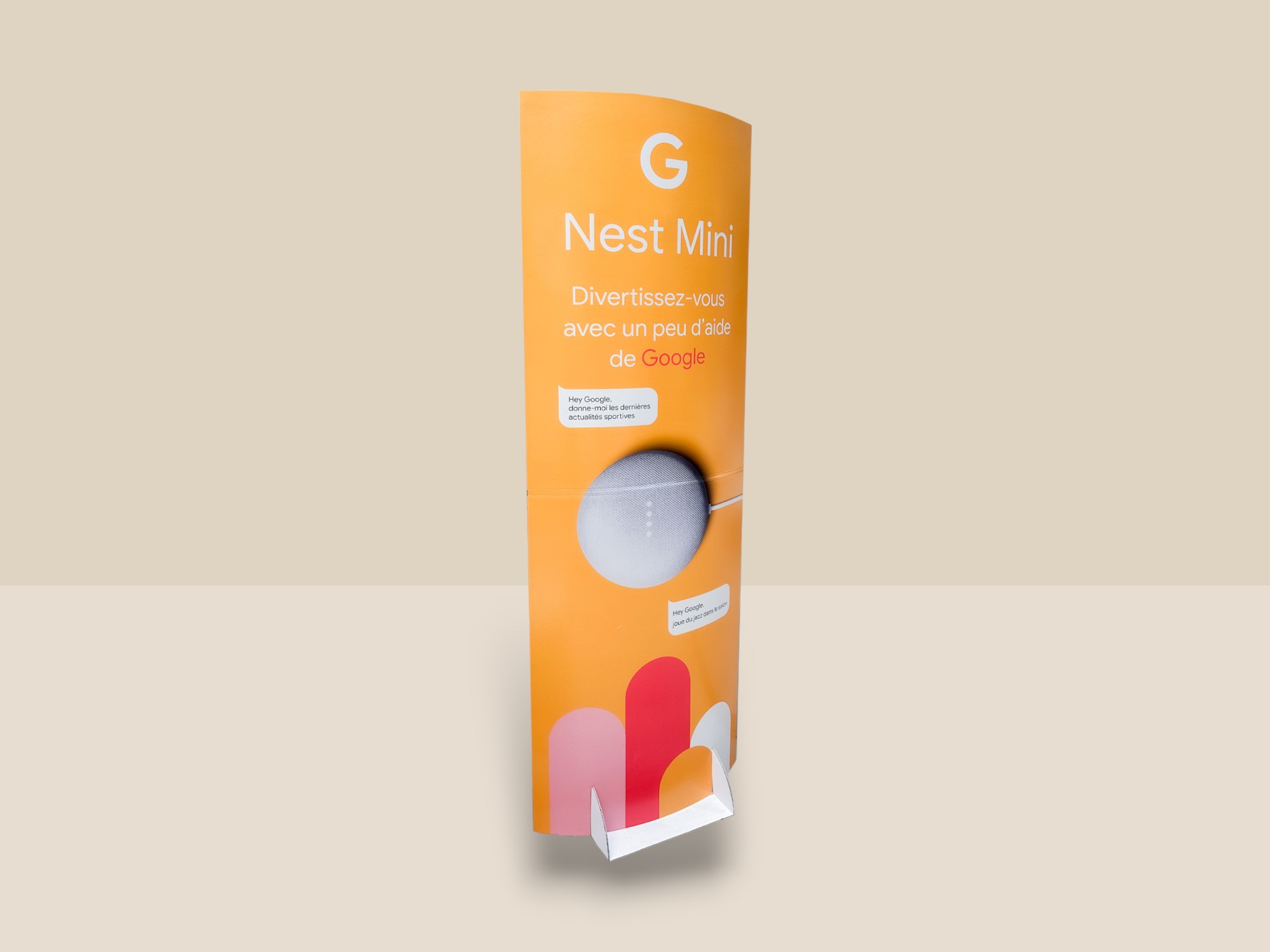 Totem en carton pour la marque Google et son produit Nest mini. La PLV est de couleur orange, rose et rouge avec le produit placé au milieu.